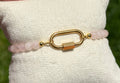 Gold bracelet with pink beads on a white cushion held by a hand against a blurred green background