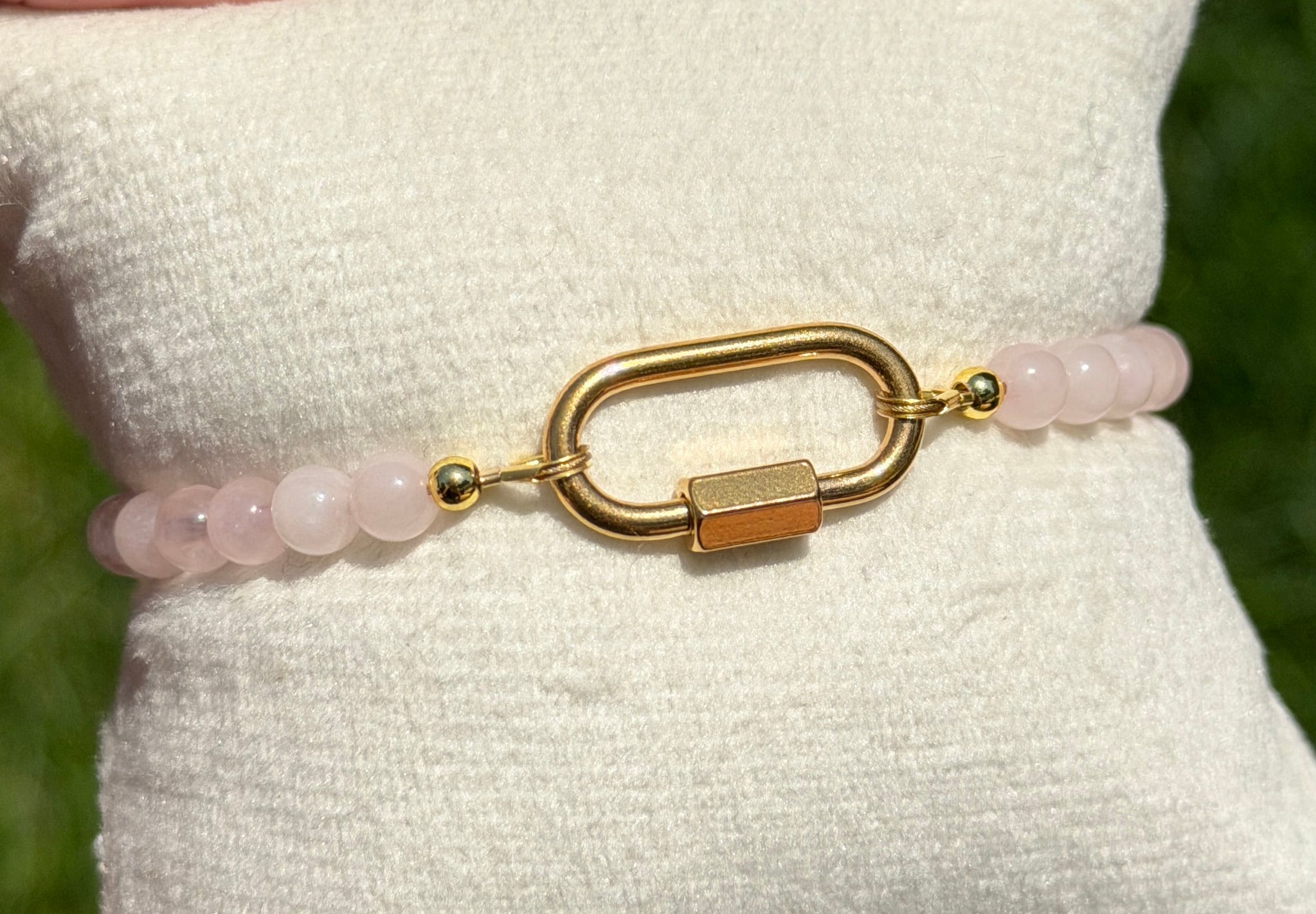 Gold bracelet with pink beads on a white cushion held by a hand against a blurred green background